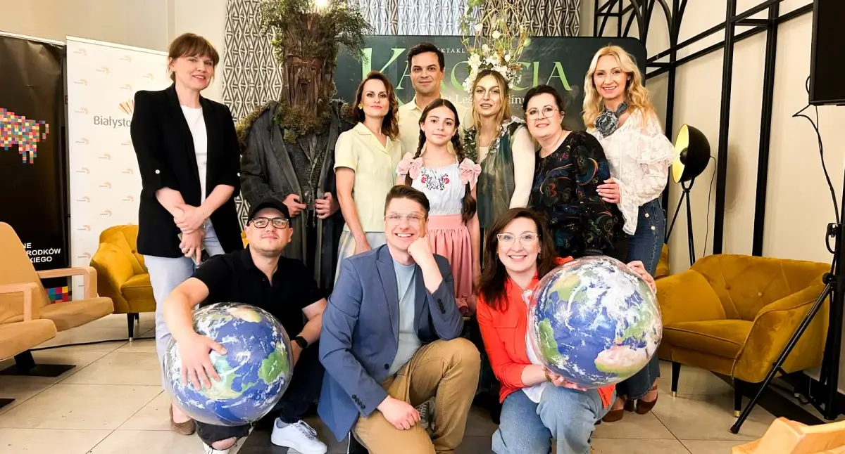 Grupa dorosłych i dziecko pozujący do wspólnego zdjęcia w przestrzeni, część osób trzyma globusy.