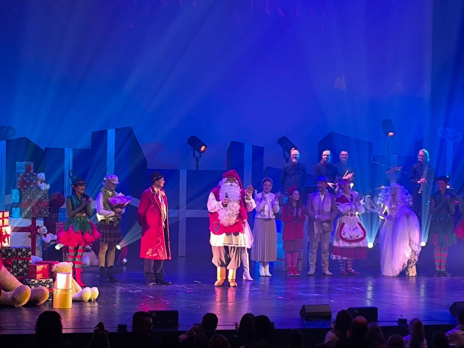 Aktorzy w kostiumach, w tym Święty Mikołaj, stoją na oświetlonej scenie podczas finału spektaklu.