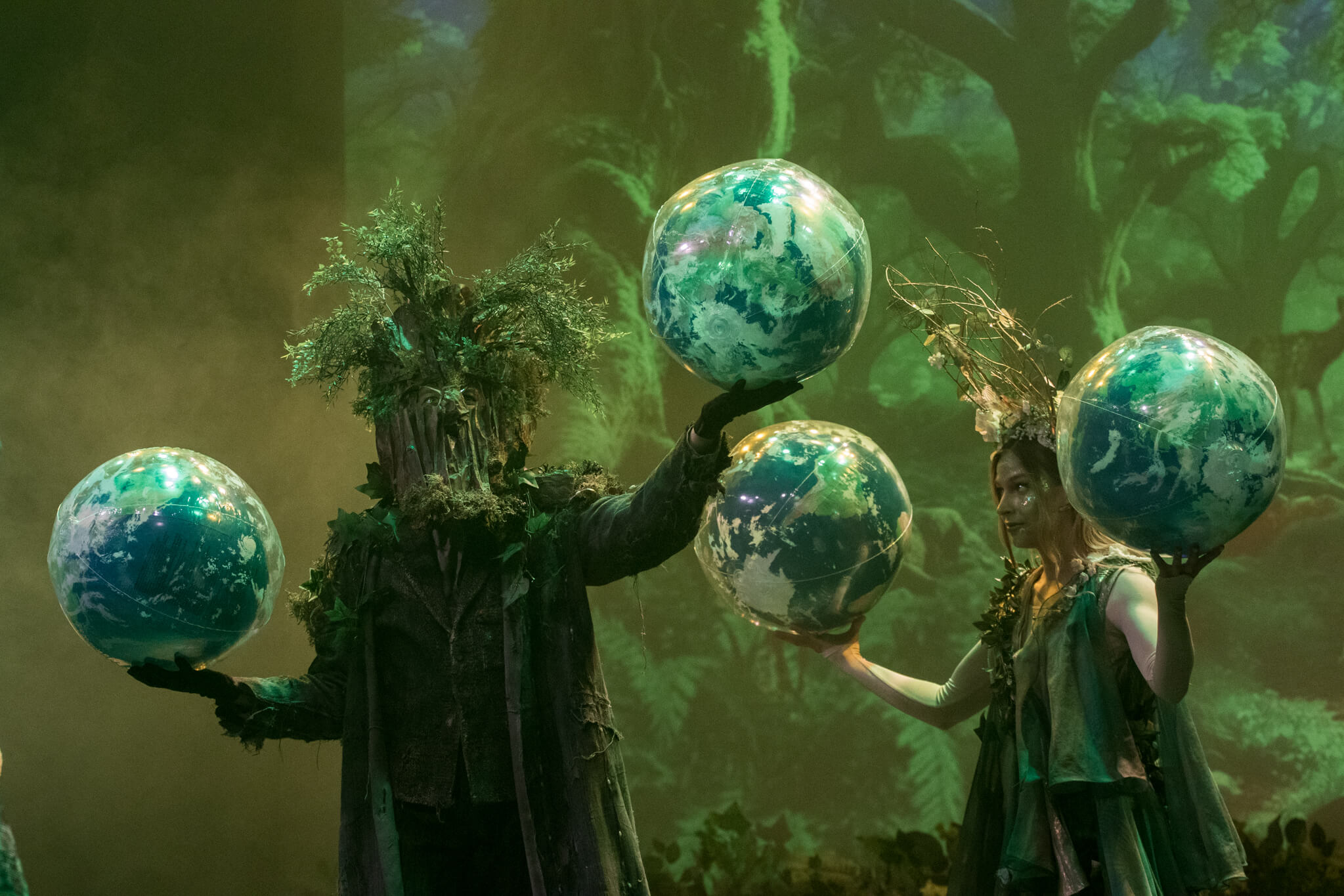Postacie w kostiumach leśnych duchów trzymają globy w spektaklu „Karolcia”.