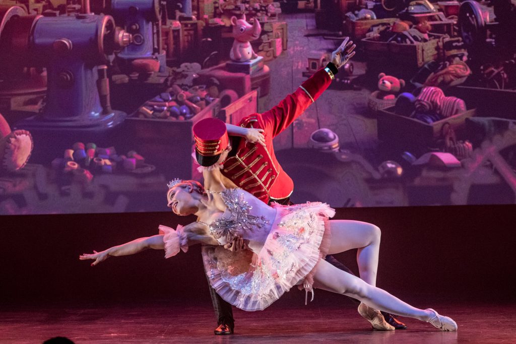 Tancerka w białej baletowej sukience i tancerz w stroju Dziadka do Orzechów wykonują taneczną figurę