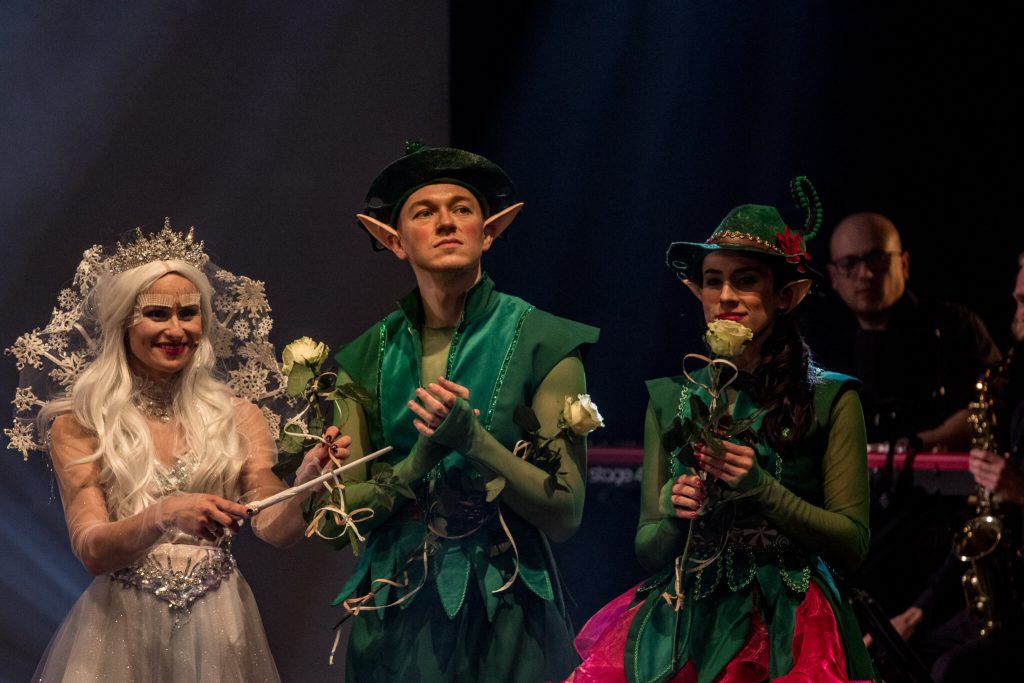 Królowa Śniegu w srebrnej koronie i dwóch elfów w zielonych strojach z białymi różami
