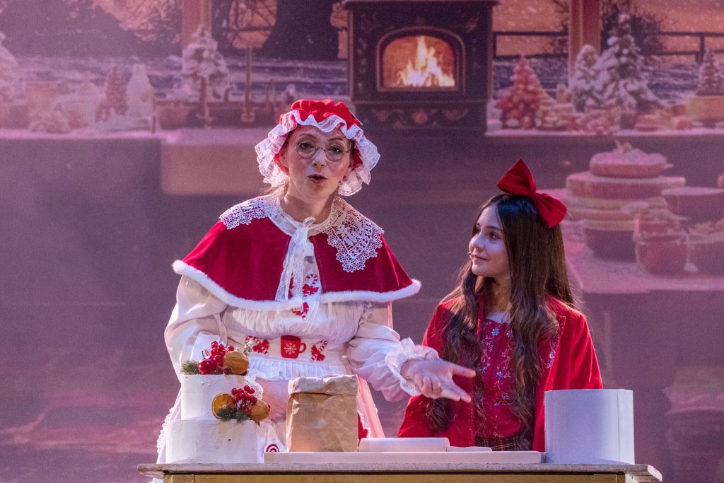 Królowa Śniegu w srebrnej sukni wykonuje dramatyczny gest na tle zimowej scenerii
