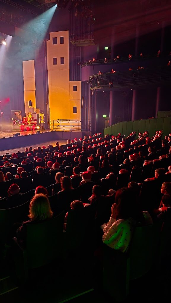 Widownia teatru z publicznością oglądającą spektakl na oświetlonej scenie