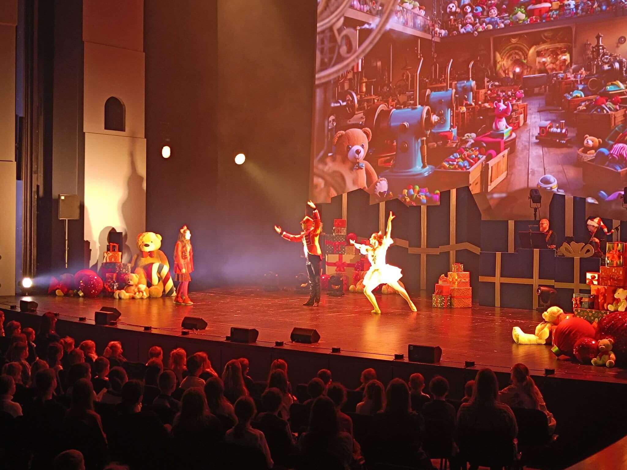 Aktorzy tańczą na scenie z dekoracjami zabawek podczas spektaklu dla dzieci.